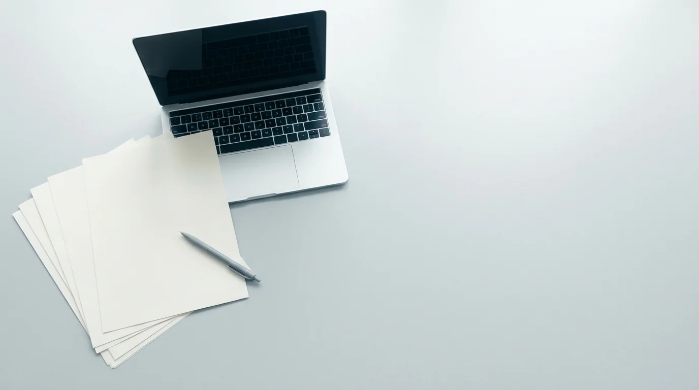 Aufgefächerte Papierunterlagen neben einem Laptop an einem aufgeräumten Arbeitsplatz